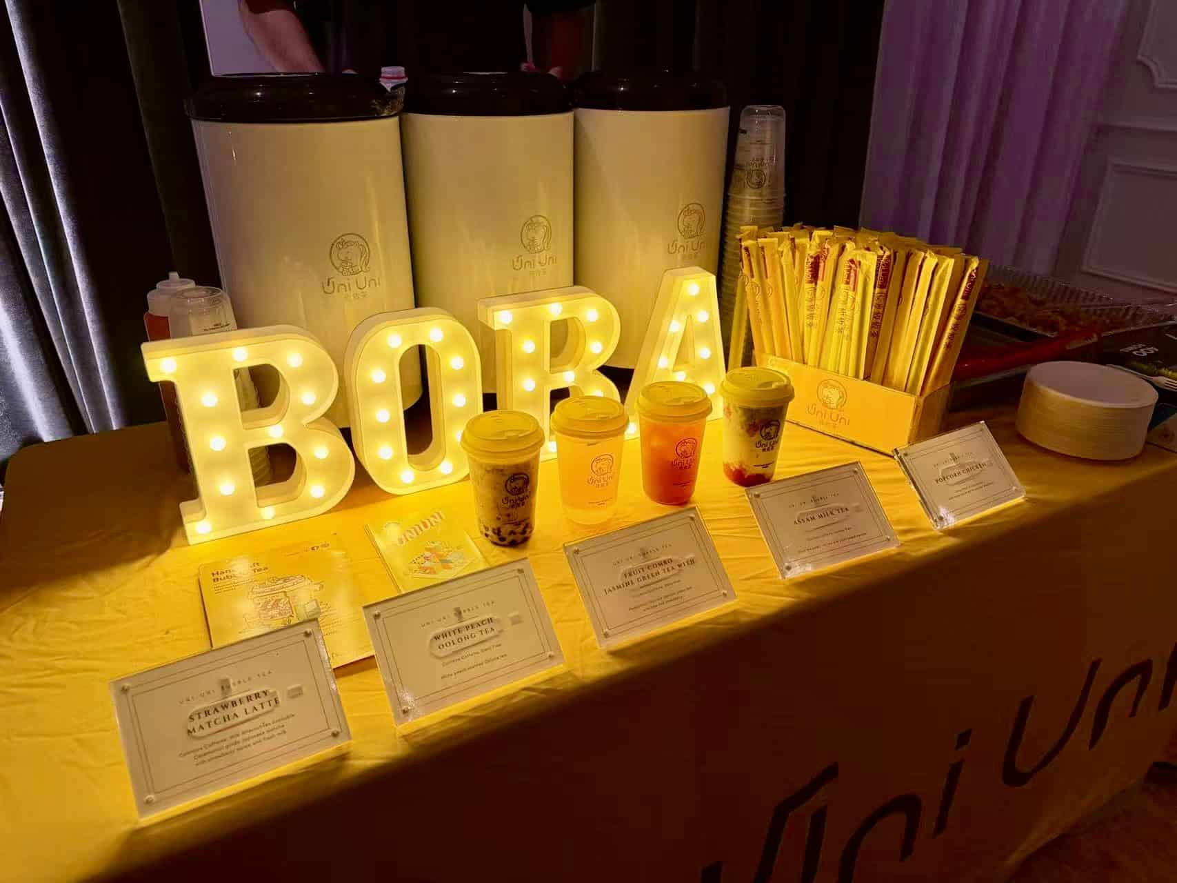 A Uni Uni boba tea station at a wedding party with drinks, straws, and menu cards on a wooden counter.